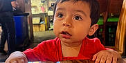 Juan joined the competition — help win amazing prizes! toddler, child, red_shirt, table, wood, indoor, restaurant, curious, face, hands, brown_hair, furniture, sombrero, background, lighting, people, person, casual, expression, candid