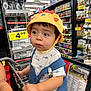 Juan joined the competition — help win amazing prizes! toddler, child, shopping_cart, grocery_store, hat, yellow_hat, lion_hat, overalls, blue_overalls, snacks, beverages, aisle, shelf, price_tag, curious, wide_eyes, clothing, person, indoor, retail