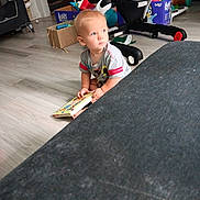 Robert joined the competition — help win amazing prizes! toddler, child, book, floor, toy, indoor, living_room, baby_gear, curious, sitting, wooden_floor, clothing, short_sleeves, light_hair, home, playtime, young_child, casual, daylight, portrait