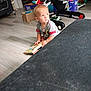 toddler, child, book, floor, toy, indoor, living_room, baby_gear, curious, sitting, wooden_floor, clothing, short_sleeves, light_hair, home, playtime, young_child, casual, daylight, portrait