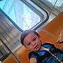 toddler, child, seat, orange_seat, public_transport, window, food, snack, blue_clothing, strap, hair, face, person, indoors, curious, messy_hair, hand, expression, young_child, transport