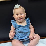 Isabella joined the competition — help win amazing prizes! baby, child, smiling, blue_outfit, headband, flower, sitting, white_cloth, dark_wall, framed_art, leaf_artwork, happy, portrait, indoor, cute, infant, skin, legs, hands, feet