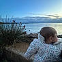 baby, child, jacket, floral_pattern, outdoor, lake, water, sky, clouds, plants, grass, rocks, nature, dusk, peaceful, scenic, portrait, infant, cold_weather, profile