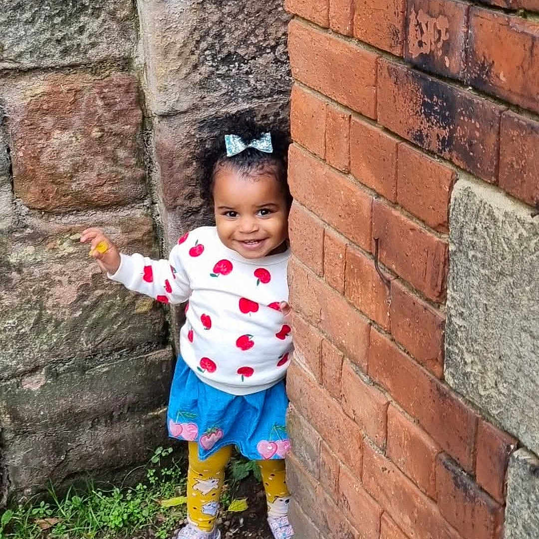 Mary joined the competition — help win amazing prizes! architecture, brick, building, child, city, clothing, face, female, footwear, girl, head, pants, person, photography, portrait, road, rock, street, urban, wall