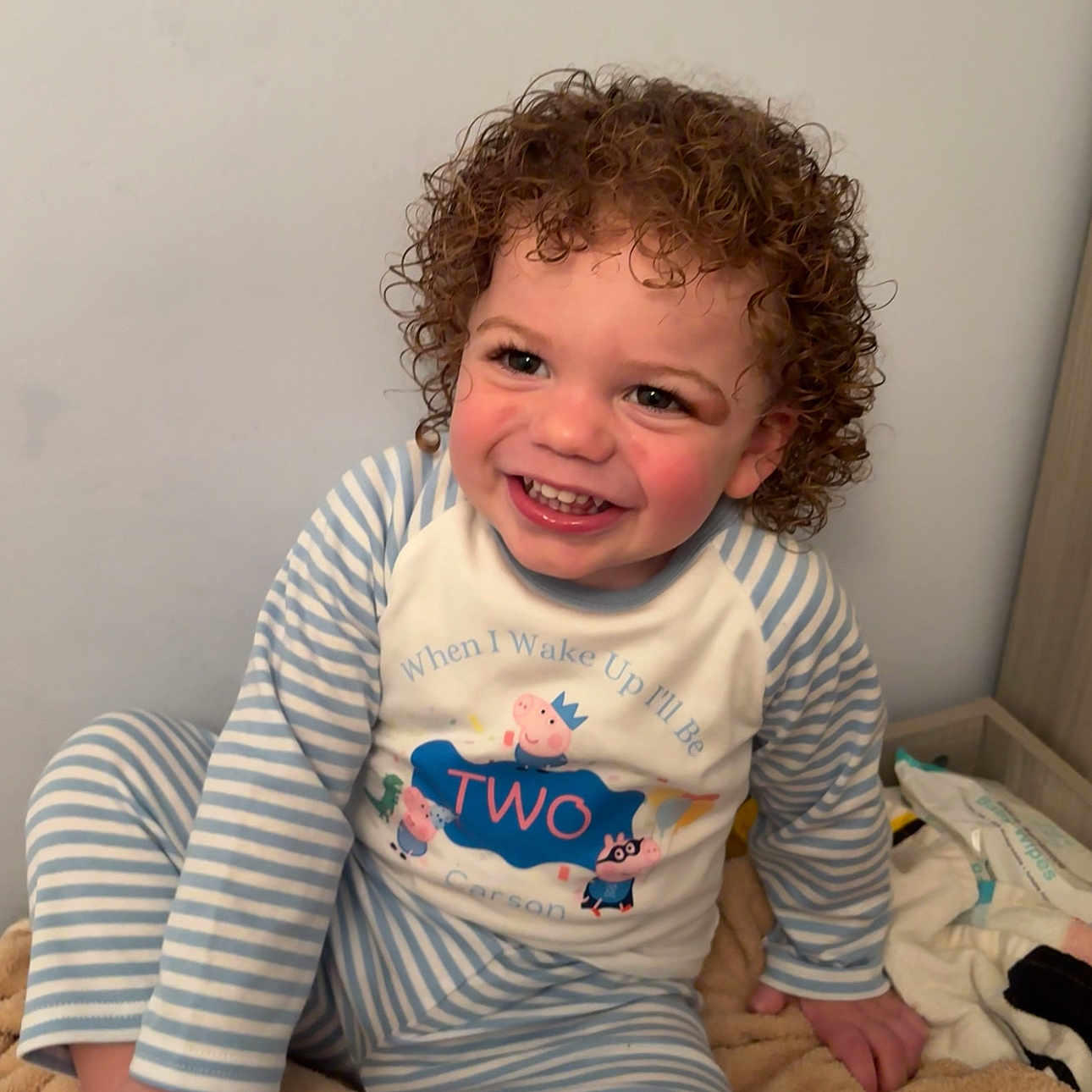 Carson-Prince is registered to the contest to win money with this photo: blanket, bright, casual, child, cozy, curly_hair, cute, face, happy, home, indoor, pajamas, person, playful, portrait, sitting, smiling, striped_clothing, toddler, young_child