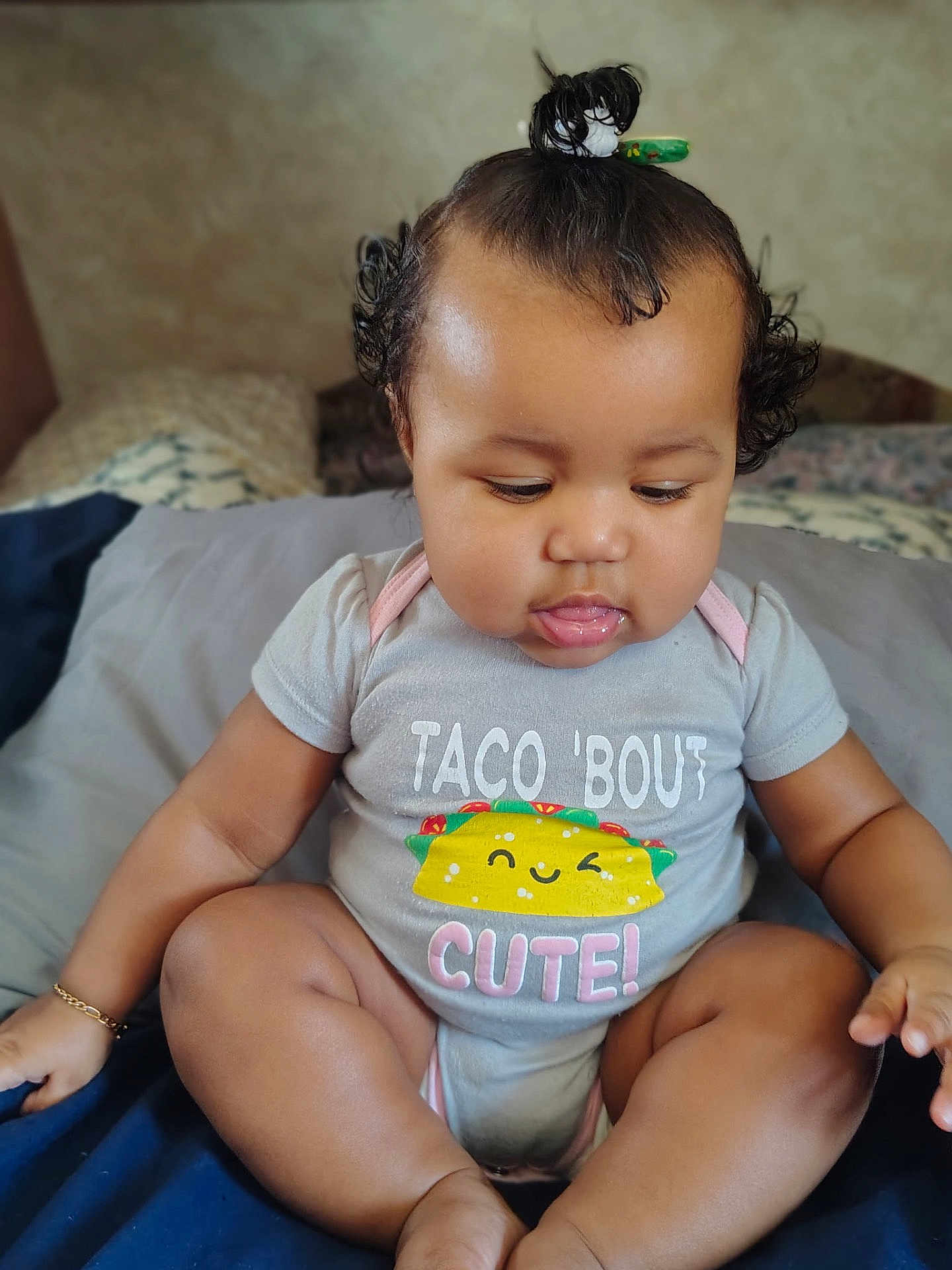 Ivy joined the competition — help win amazing prizes! baby, infant, child, onesie, taco_graphic, cute, sitting, bed, blanket, pillow, hair_topknot, curly_hair, bracelet, chubby_legs, portrait, indoors, playful, tongue_out, smiling, close_up