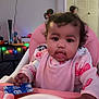 baby, child, highchair, bib, pink, pigtails, curly_hair, face, eyes, mouth, toy, tray, indoor, living_room, television, decorative_lights, furniture, hand, clothing, feeding