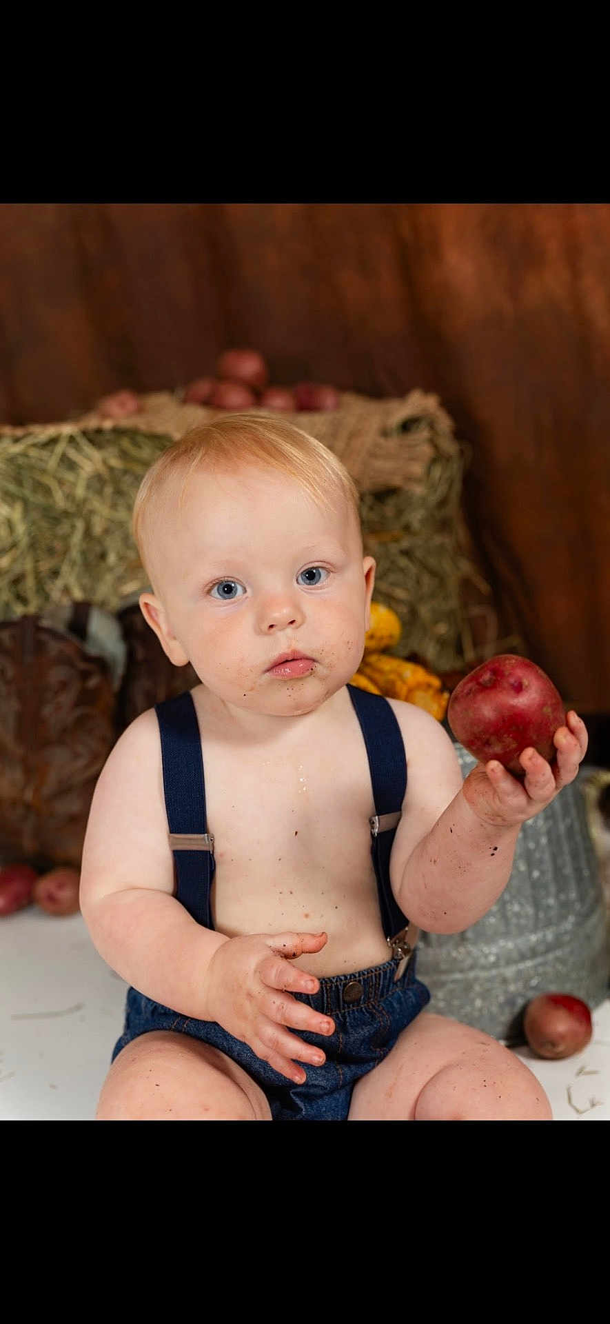 Zion joined the competition — help win amazing prizes! baby, child, potato, dirt, face, hand, blue_eyes, denim_shorts, suspenders, bare_chest, boots, hay, rustic, farm, background, sitting, curious, indoor, person, portrait