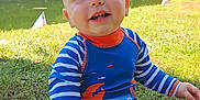 Zion joined the competition — help win amazing prizes! baby, child, smiling, outdoor, grass, pond, trees, sunlight, blue_swimsuit, orange_details, striped_sleeves, sitting, happy, nature, water, summer, cute, person, young_child, playful