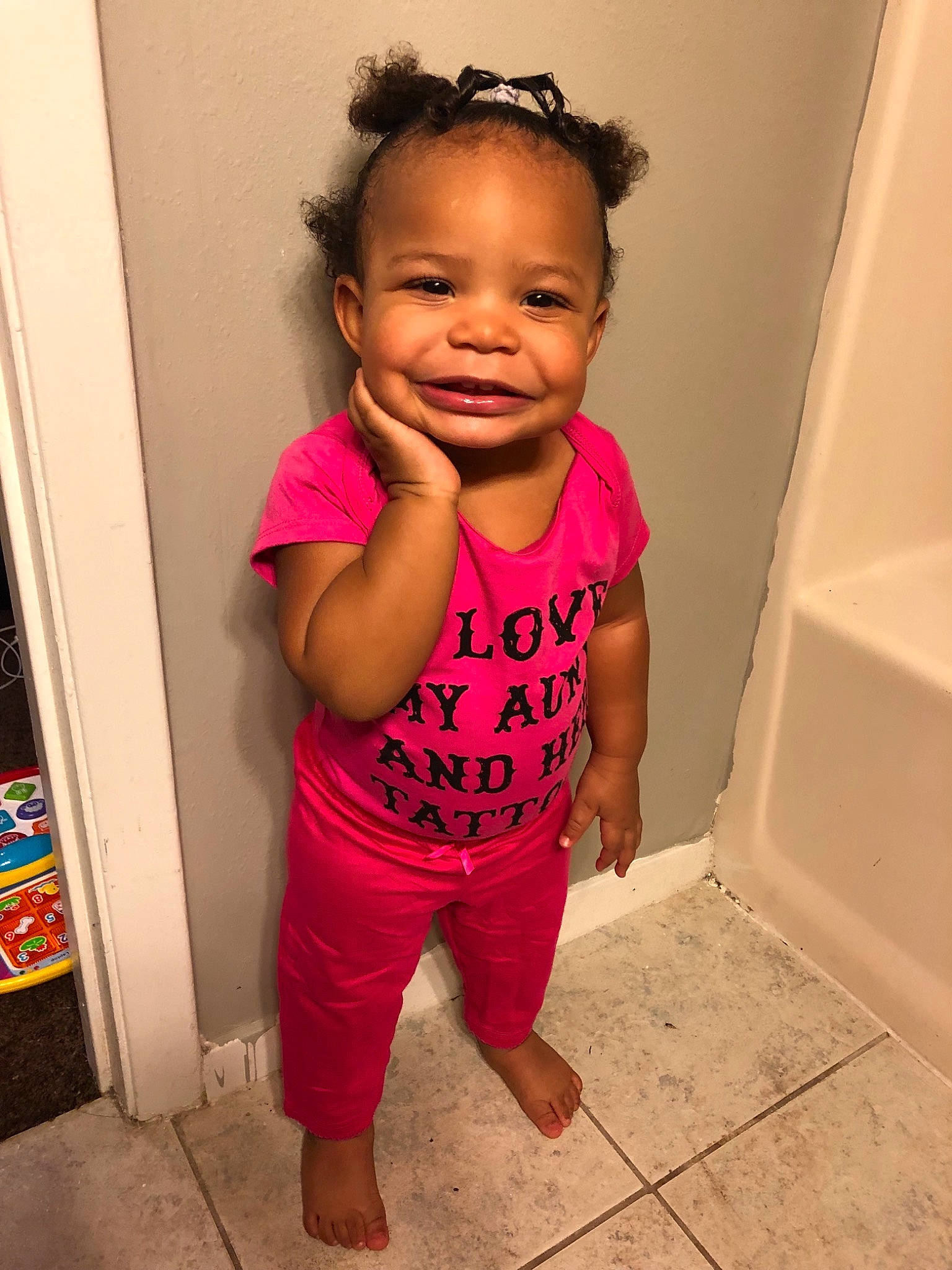 Lola is registered to the contest to win money with this photo: baby, baby_toddler_clothing, cheek, child, daughter, face, hair, hairstyle, head, joy, person, pink, room, shoulder, skin, smile, standing, toddler