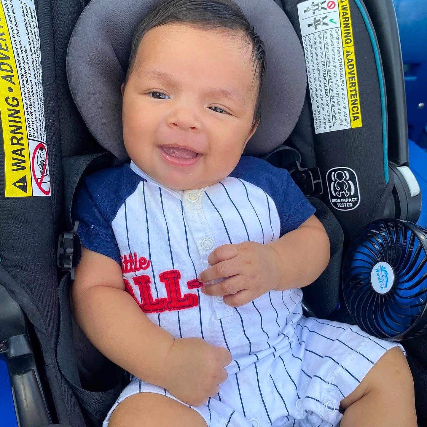 Jefe Noel is registered to the contest to win money with this photo: baby, buttoned, car_seat, casual_outfit, child, clothing, cute, fan, happy, head_support, indoor, infant, person, portrait, safety_labels, seat_belt, shorts, sitting, smiling, young