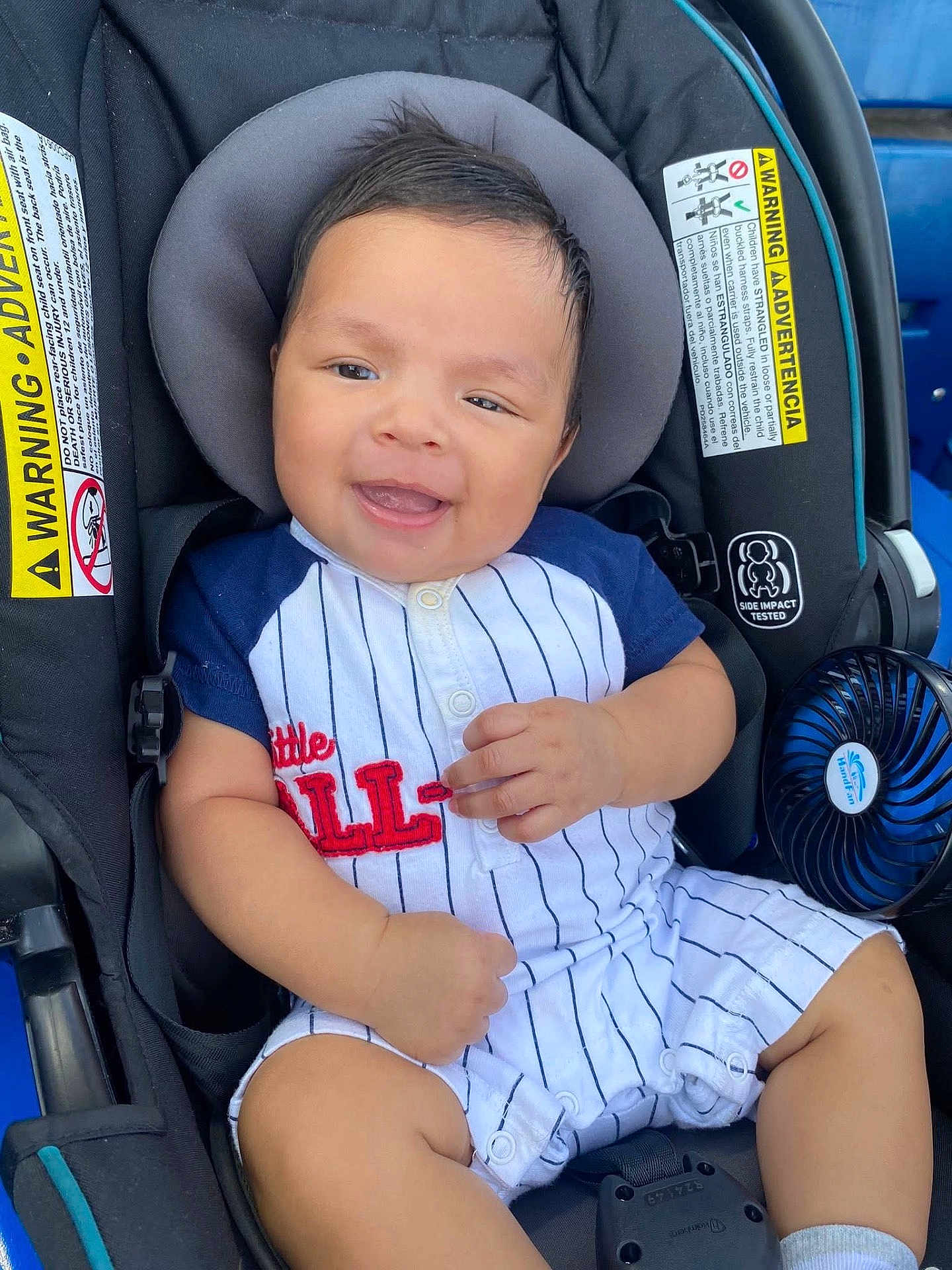 Jefe Noel is registered to the contest to win money with this photo: baby, child, car_seat, smiling, infant, clothing, sitting, safety_labels, fan, cute, portrait, happy, young, casual_outfit, indoor, person, seat_belt, head_support, shorts, buttoned