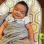 baby, blanket, cushion, pattern, wood_floor, smile, face, infant, clothing, indoor, person, child, seat, comfort, relax, happy, cute, young, resting, soft