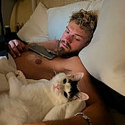 Quincy Nox is registered to the contest to win money with this photo: animal, bed, blanket, bracelet, cat, comfort, cozy, curly_hair, feline, human, indoor, man, nighttime, pet, phone, pillow, relaxing, resting, shirtless, sleepy