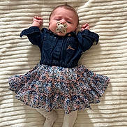 Mïa a rejoint le concours — aidez-le/la à gagner de superbes lots ! baby, bed, blanket, clothing, cute, denim_jacket, face, floral_skirt, hands_up, head, indoors, infant, lying_down, newborn, pacifier, patterned_fabric, portrait, smiling, soft_texture, tights