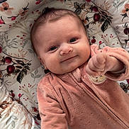 Mïa a rejoint le concours — aidez-le/la à gagner de superbes lots ! baby, infant, smile, onesie, pink_clothing, floral_bedding, pillow, plush_toy, hand, face, eyes, cheeks, newborn, portrait, lying_down, cozy, nursery_item, patterned_fabric, cute, baby_bedding