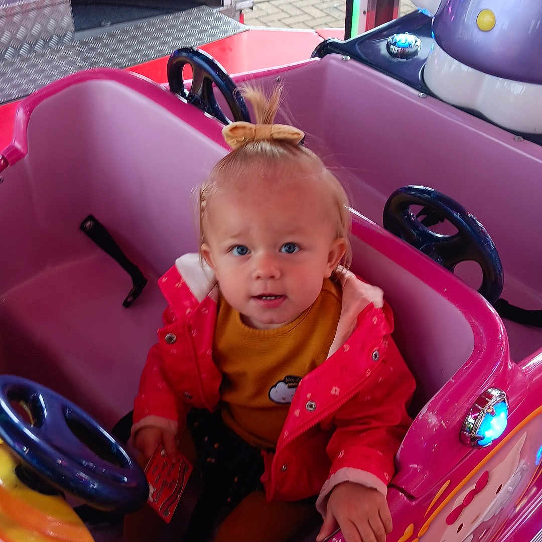 Lizya participe au concours pour gagner de l'argent avec cette photo : amusement_park, blue_eyes, car, child, cute, fairground, hello_kitty, indoor, kiddie_ride, pink, playful, portrait, red_jacket, ride, seat, small_hair_bow, steering_wheel, toddler, toy, yellow_shirt