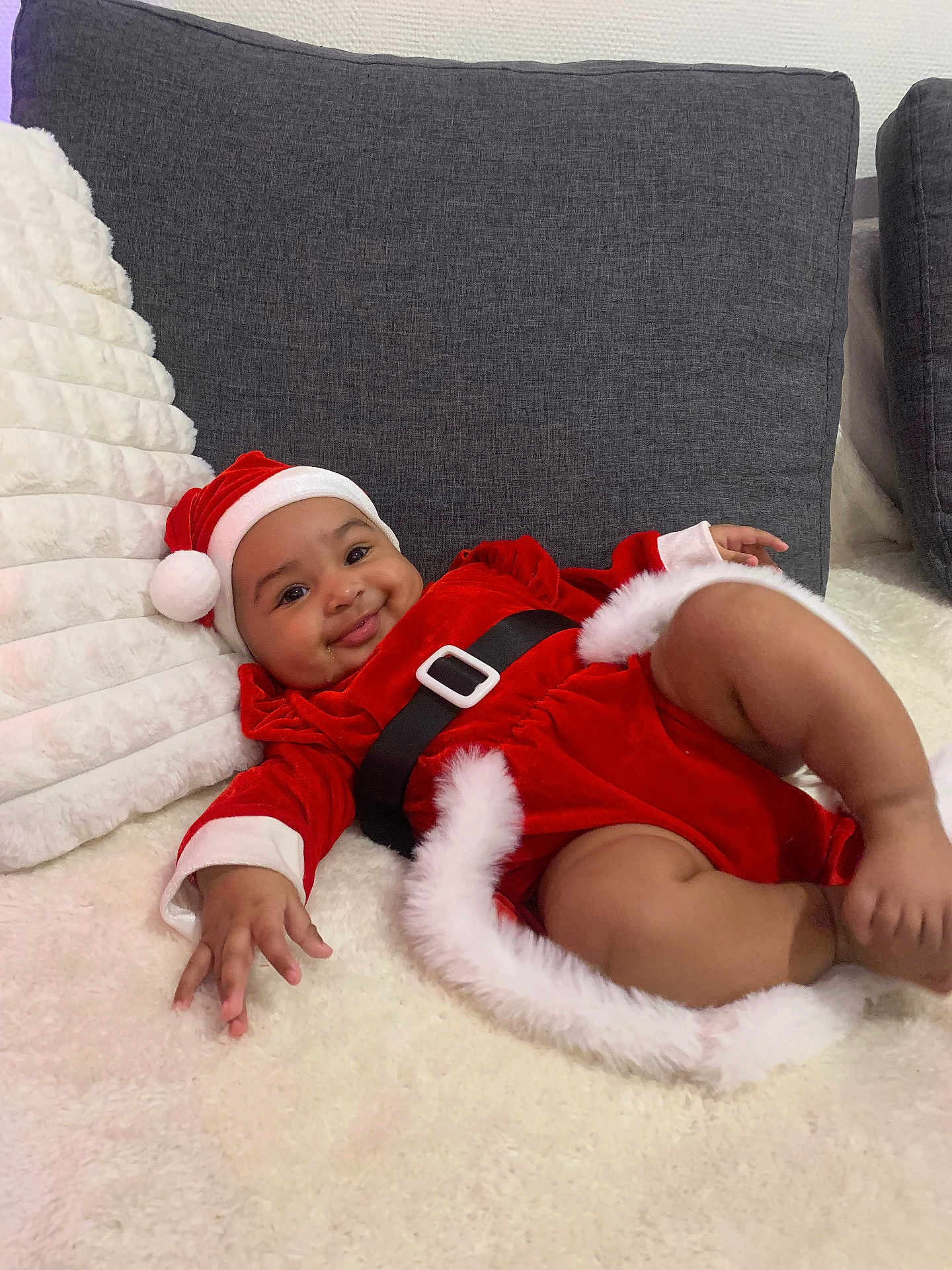 Azzura a rejoint le concours — aidez-le/la à gagner de superbes lots ! baby, infant, child, santa_hat, christmas_costume, red_clothing, white_fur_trim, black_belt, couch, cushion, blanket, smile, happy, indoors, portrait, cute, holiday, festive, relaxing, person