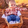 baby, casual_clothing, child, curious, cute, daytime, dirt_ground, infant, jeans, nature, outdoor, plaid_shirt, portrait, relaxed, scenic_background, sitting, sunlight, tree_trunk, wicker_basket, young_child