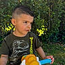child, boy, toy, ride_on_toy, motorcycle_toy, outdoor, garden, greenery, grass, bushes, casual_clothing, short_hair, portrait, daylight, play, summer, cute, young, tshirt, thinking
