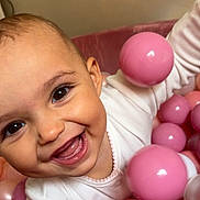 Alana is registered to the contest to win money with this photo: baby, smiling, child, face, pink, balls, ball_pit, white_clothing, happy, play, cute, infant, closeup, indoors, cheerful, skin, eyes, mouth, tongue, fun