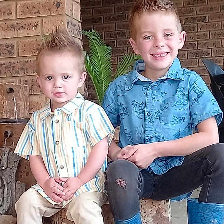 Delano is registered to the contest to win money with this photo: children, brothers, boys, portrait, smiling, sitting, porch, brick_wall, outdoor, spiky_hair, blue_shirt, striped_shirt, boots, sneakers, plant, home, family, casual_clothing, young, happy
