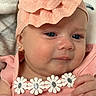 baby, infant, child, portrait, face, blue_eyes, pink_outfit, peach_bow, headband, daisy, floral_detail, rosy_cheeks, sitting, close_up, indoors, soft_blanket, fashion, hands, jewelry, smiling