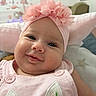 baby, infant, child, smiling, portrait, close_up, pink, flower_headband, headband, onesie, floral_clothing, buttons, indoors, bedroom, bed, pillows, blanket, home, happy, face