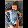 baby, smiling, blue_romper, blanket, infant, lying_down, cute, happy, child, indoors, one_person, casual_clothing, portrait, skin, head, arms, legs, comfortable, young_child, soft_texture