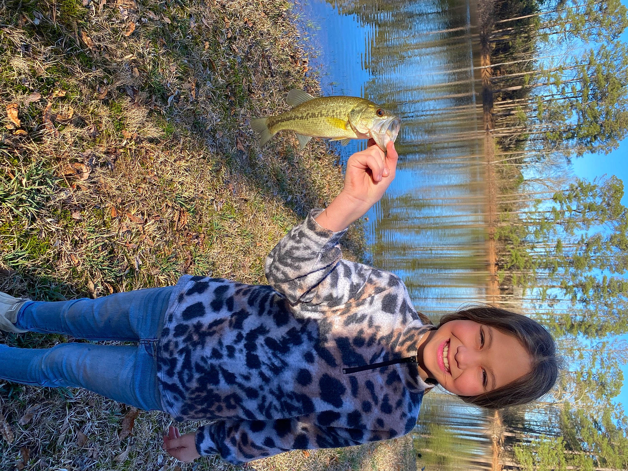 Piper is registered to the contest to win money with this photo: child, fun, grass, happy, human_leg, joy, lake, landscape, leisure, pattern, people_in_nature, person, plant, play, recreation, reflection, sitting, thigh, tree, water