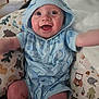 baby, child, blue_clothing, hoodie, smiling, happy, indoor, cushion, animal_print, pattern, cute, infant, person, sitting, reaching, playful, face, eyes, mouth_open, joyful