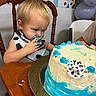balloons, birthday_cake, blue_frosting, cake, celebration, child, clothing, cowboy_theme, curious, face, food, frosting, hand, indoor, messy_face, party_decoration, person, table, toddler, wooden_chair