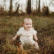 Kash is registered to the contest to win money with this photo: baby, child, grass, outdoor, nature, trees, smiling, autumn, field, leaves, sitting, cute, portrait, young, sunlight, warm, forest, casual_clothing, happy, baby_boy