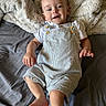 Kash is registered to the contest to win money with this photo: baby, child, infant, bed, blanket, overalls, white_shirt, smile, happy, skin, foot, hand, face, head, person, indoor, fabric, texture, cozy, relaxed