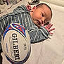 baby, infant, striped_clothing, rugby_ball, gilbert, lying_down, indoor, white_cloth, newborn, hand, face, head, sports_equipment, curious, soft_lighting, mirror_reflection, closeup, person, child, casual