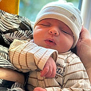 Leny a rejoint le concours — aidez-le/la à gagner de superbes lots ! newborn, baby, sleeping, hat, striped_clothing, hand, arm, person, closeup, window, blurred_background, indoor, cozy, soft_lighting, peaceful, infant, cute, resting, portrait, toddler