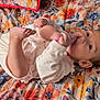 baby, infant, foot, hand, blanket, floral_pattern, lying_down, clothing, cute, face, skin, person, indoors, comfort, playful, young_child, expression, looking, colorful, bedspread