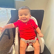 Ezeriah is registered to the contest to win money with this photo: baby, child, high_chair, red_clothing, smile, indoor, window, natural_light, carpet, table, chair, happy, person, infant, sitting, short_hair, skin, arm, legs, casual