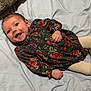 baby, infant, smiling, floral_dress, blanket, lying_down, happy, child, cute, indoors, soft_texture, face, hands, eyes, clothing, person, young, cheerful, newborn, cozy