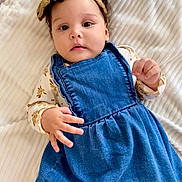 Antonella is registered to the contest to win money with this photo: baby, blanket, child, clothing, curly_hair, cute, denim_dress, face, headband, human, indoor, infant, laying_down, looking_at_camera, portrait, skin, small_hands, soft_texture, white_background, young_child