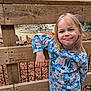 child, girl, smile, blonde_hair, floral_sweater, wooden_fence, outdoor, nature, wallabies, animals, pond, trees, autumn_leaves, casual_pose, playful, cute, young, park, daylight, happy
