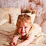 child, girl, blonde_hair, smiling, bed, textured_blanket, pillow, indoor, portrait, happy, face, hands, cozy, soft_lighting, home_interior, casual_clothing, young, cute, relaxed, playful