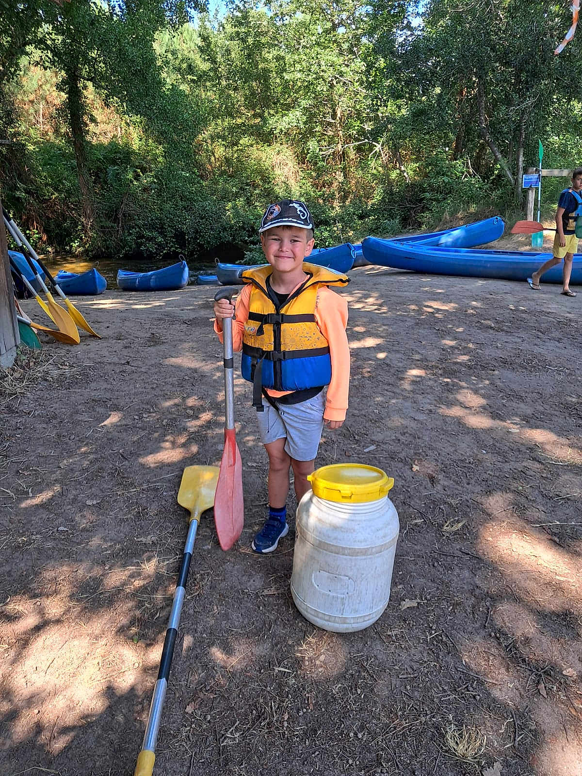 Valentin participe au concours pour gagner de l'argent avec cette photo : child, boy, paddle, life_jacket, cap, canoe, riverbank, trees, outdoor, summer, smile, adventure, nature, water_sport, sand, sunlight, play, recreation, fun, daytime