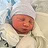 Omari is registered to the contest to win money with this photo: newborn, baby, sleeping, infant, portrait, face, closed_eyes, knit_hat, striped_hat, blanket, swaddled, white_clothing, hospital, bed, cozy, peaceful, indoors, close_up, resting, photography