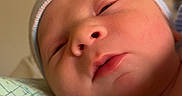 Omari is registered to the contest to win money with this photo: newborn, baby, infant, child, sleepy, portrait, face, hospital, blanket, swaddle, hat, cap, striped_clothing, blue, close_up, indoors, cozy, lying_down, head, photograph