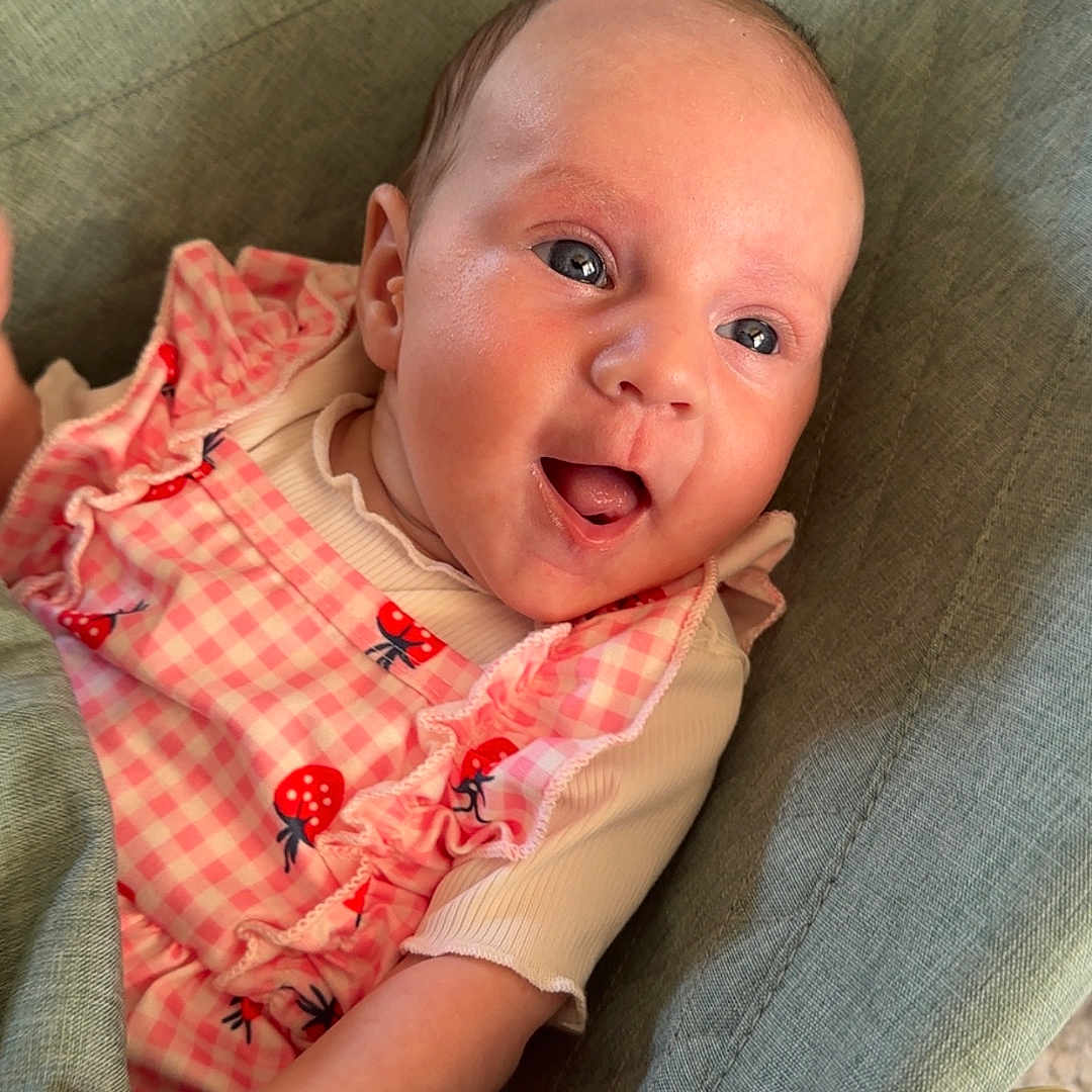 Esmae is registered to the contest to win money with this photo: baby, checkered, child, clothing, cushion, cute, expression, eyes, fabric, face, hand, happy, indoors, infant, pink, portrait, seat, smiling, strawberry_pattern, young