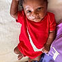 baby, infant, child, red_onesie, curly_hair, lying_down, white_blanket, person, shorts, purple_shirt, hand_raised, fingers_spread, skin, cute, closeup, indoors, soft_light, casual_clothing, resting, portrait