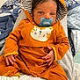 Jaïlan participe au concours pour gagner de l'argent avec cette photo : baby, pacifier, hood, orange_clothing, striped_lining, hand, feet, blanket, bed, person, infant, sleepwear, fabric, cute, resting, indoor, comfort, portrait, newborn, soft