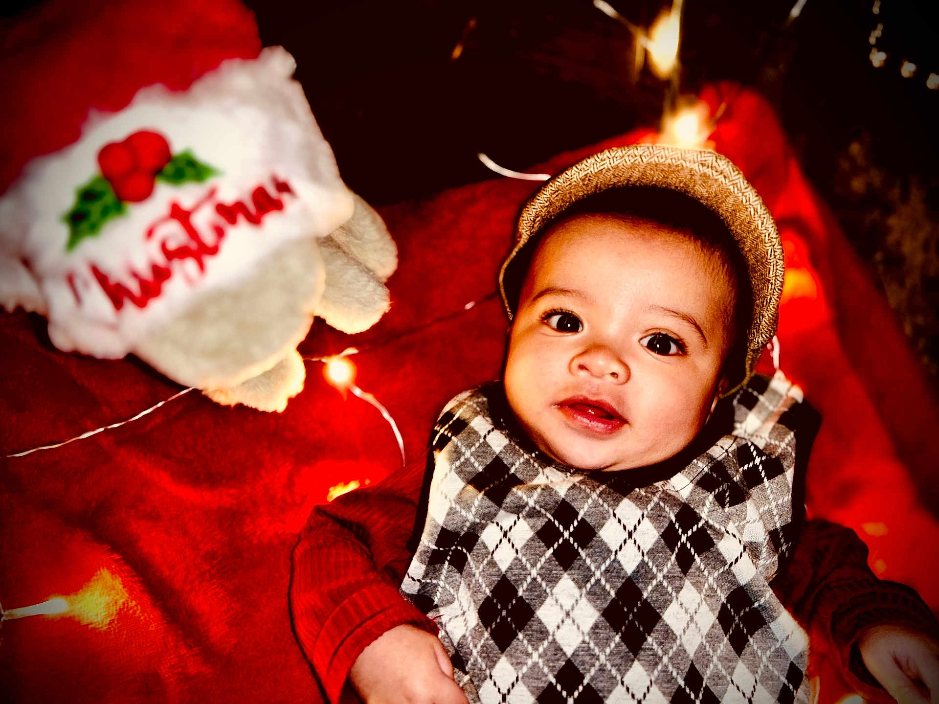 Khylae joined the competition — help win amazing prizes! baby, child, face, hat, argyle_sweater, red_clothing, blanket, christmas, holiday_lights, festive, smiling, indoors, cute, infant, portrait, cozy, toy, decoration, warm_lighting, holiday_theme