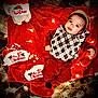Khylae is registered to the contest to win money with this photo: baby, child, christmas, holiday, festive, lights, red_blanket, stockings, plaid_clothing, infant, floor, cozy, cute, smiling, warm_lighting, indoors, celebration, decorations, person, portrait